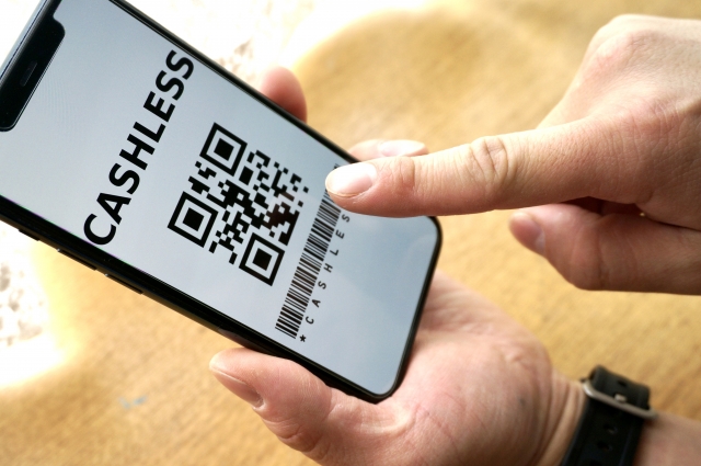 給油機の前でスマホを取り出してモバイルエネキーを使おうとしている様子。スマホ操作や読み取りの手間を表現。